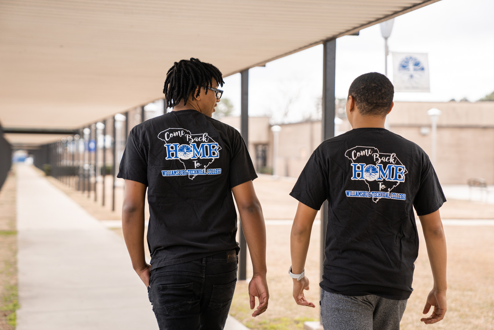 two people walking wearing "Come Back Home" t-shirts