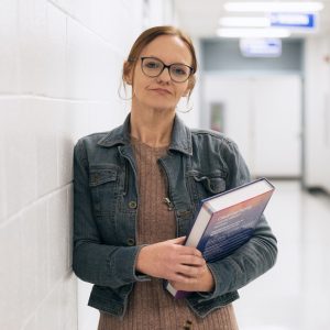Person standing in a hallway holding a textbook